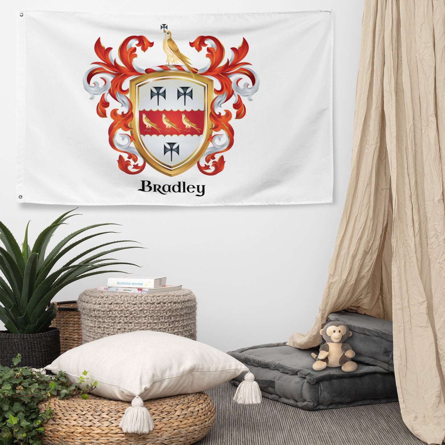 A white wall flag featuring a personalized family crest with the name 'Bradley' in black script, displayed in a styled bedroom setting with a canopy, pillows, and plants.