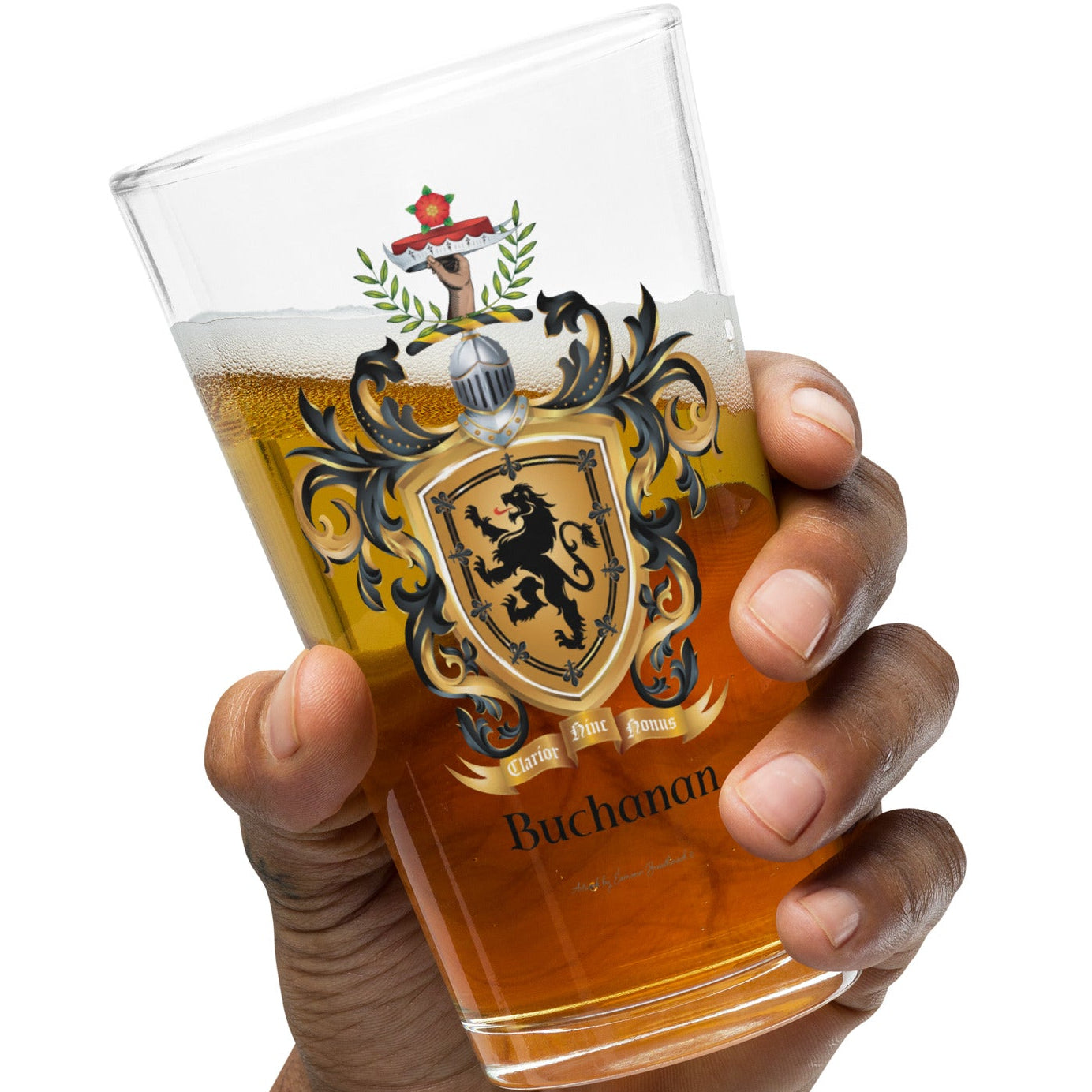 A hand holding a clear pint glass filled with amber beer, featuring a printed black, gold, and red crest with the name 'Buchanan' near the bottom, against a plain white background.