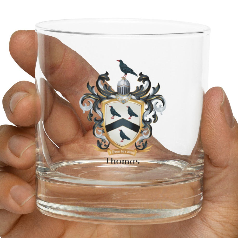 Hand holding a clear Thomas _Family Crest Rocks Glass design on a white background