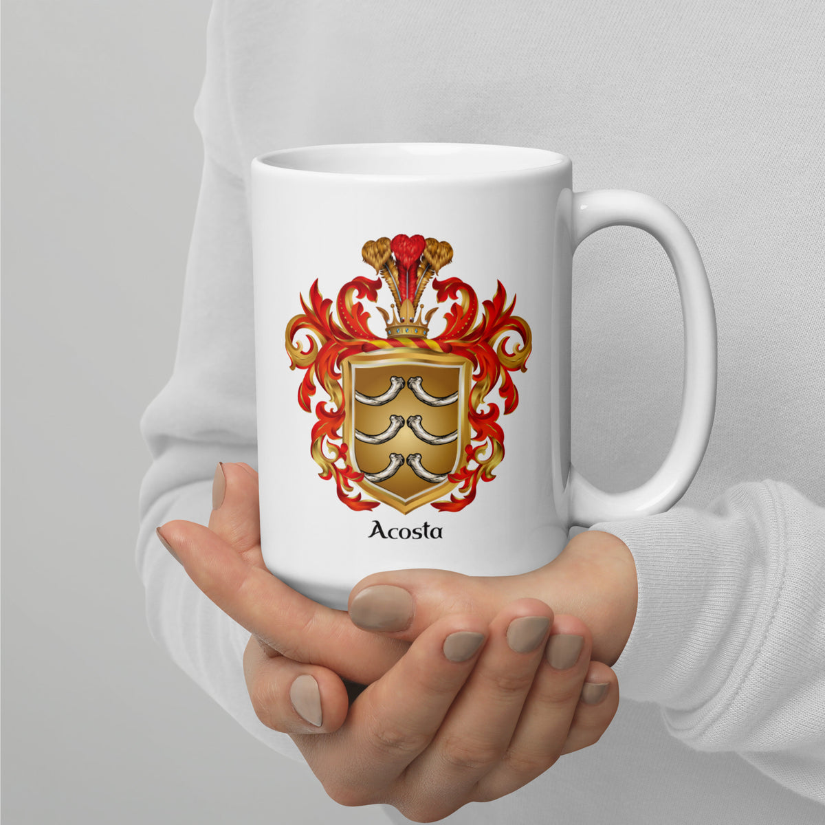 A white ceramic mug with a detailed Acosta family crest printed on the front, held by a person's hands wearing a white long-sleeve shirt against a neutral gray background.
