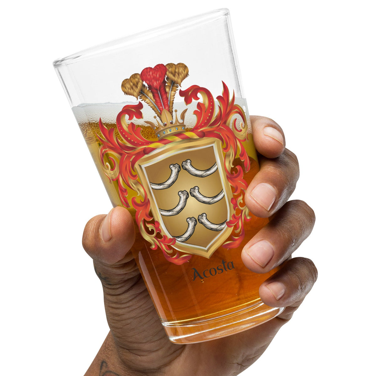 A hand holding a clear pint glass filled with amber beer, featuring a printed heraldic coat of arms with red, gold, and silver details and the name 'Acosta' near the bottom, against a plain white background.