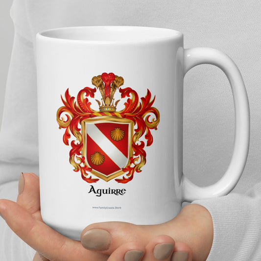 A person in a white long-sleeve top holds a white ceramic mug with a red, gold, and white Aguirre coat of arms printed on the front, set against a neutral light gray background.