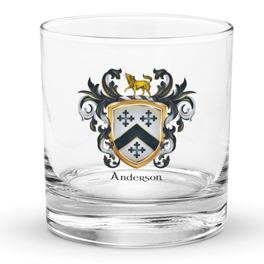 A clear rocks glass with an Anderson Family Crest featuring a black chevron and three black crosses and a hound on the crest above the shield all pictured against a white background.