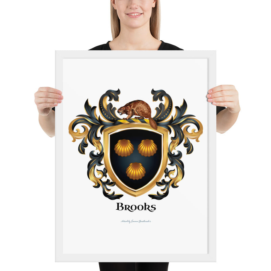 A woman standing in a white background, holding a white framed print of the Brooks Coat of Arms featuring 3 clam shells on a black shield with a beaver on the crest of the shield.