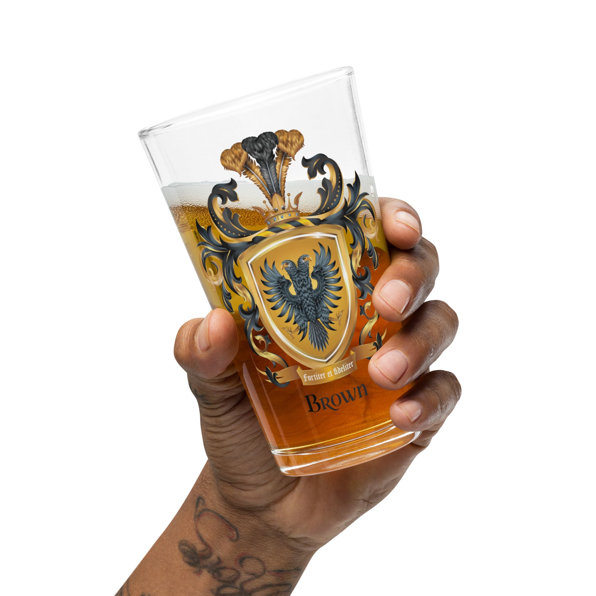 Hand holding a pint sized beer clear glass with a detailed illustration of the Brown Family Crest featuring a black two-headed eagle pictured against a clear white background