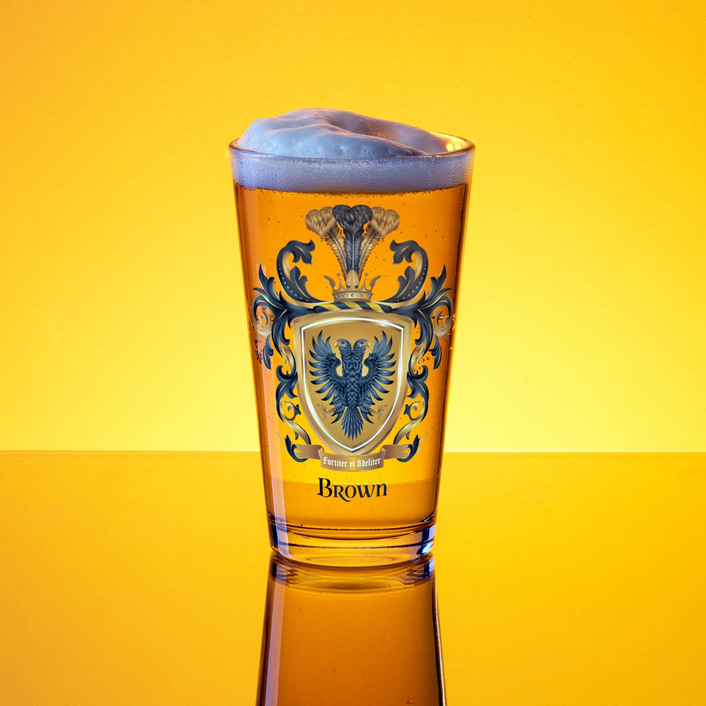 A pint sized beer clear glass with a detailed illustration of the Brown Family Crest featuring a black two-headed eagle on a yellow background