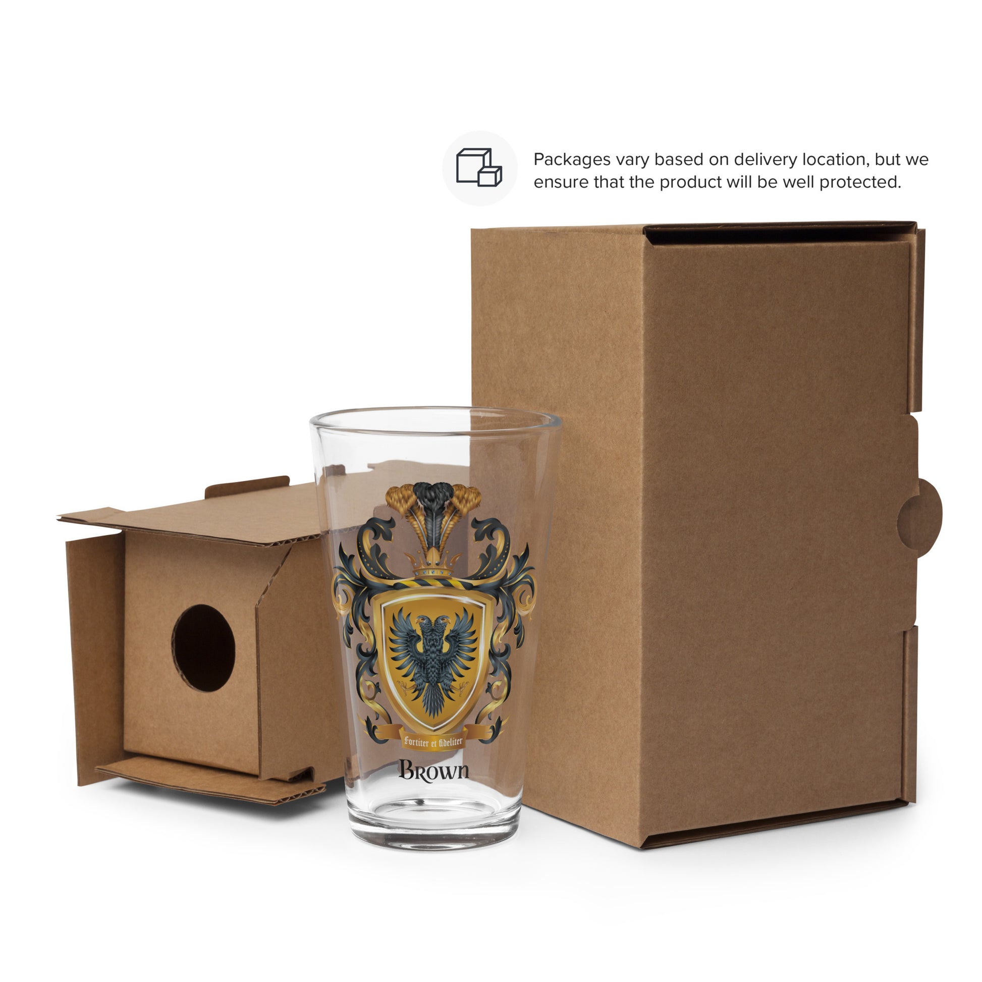 A pint sized beer clear glass with a detailed illustration of the Brown Family Crest featuring a black two-headed eagle pictured next to a cardboard box on a white background
