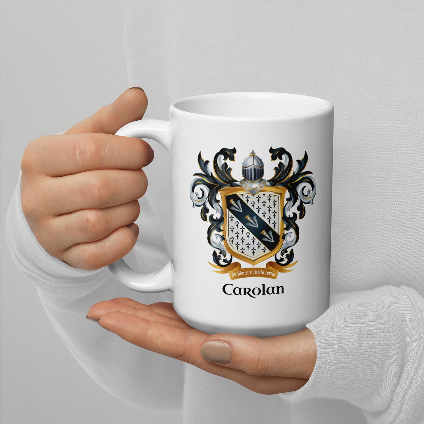 A person in a white long-sleeve top holds a white ceramic mug with a detailed family crest and the name 'Carolan' printed on the front, set against a plain light gray background.