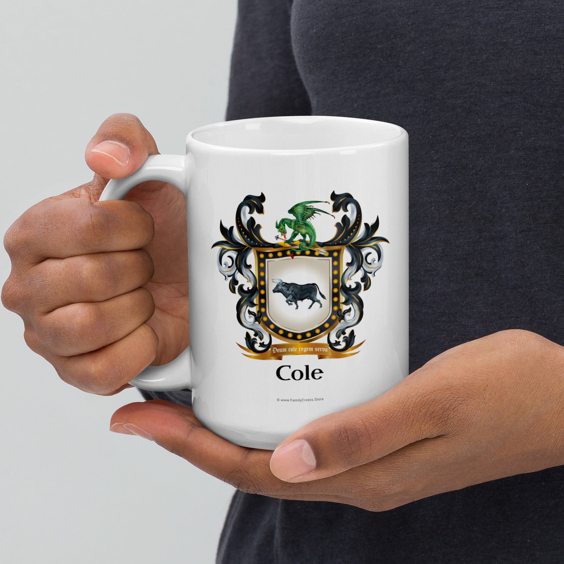 Person holding a white mug with a Cole-Family-Crest coat of arms design on a light gray background