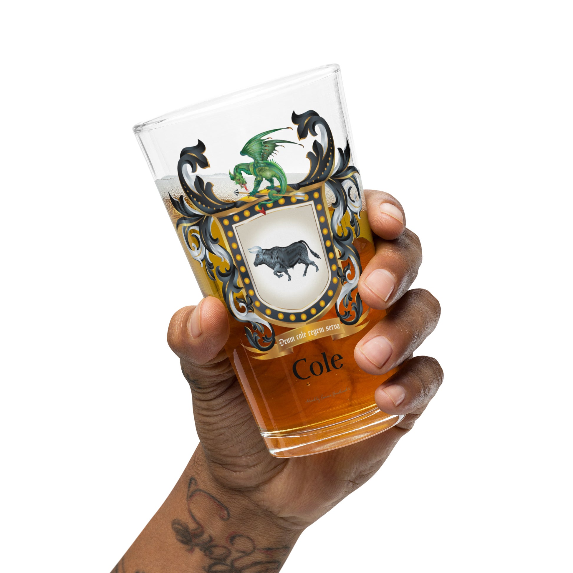 Hand holding a glass of beer with a Cole family coat of arms showing a black bull and a dragon on the front of the glass  on a white background