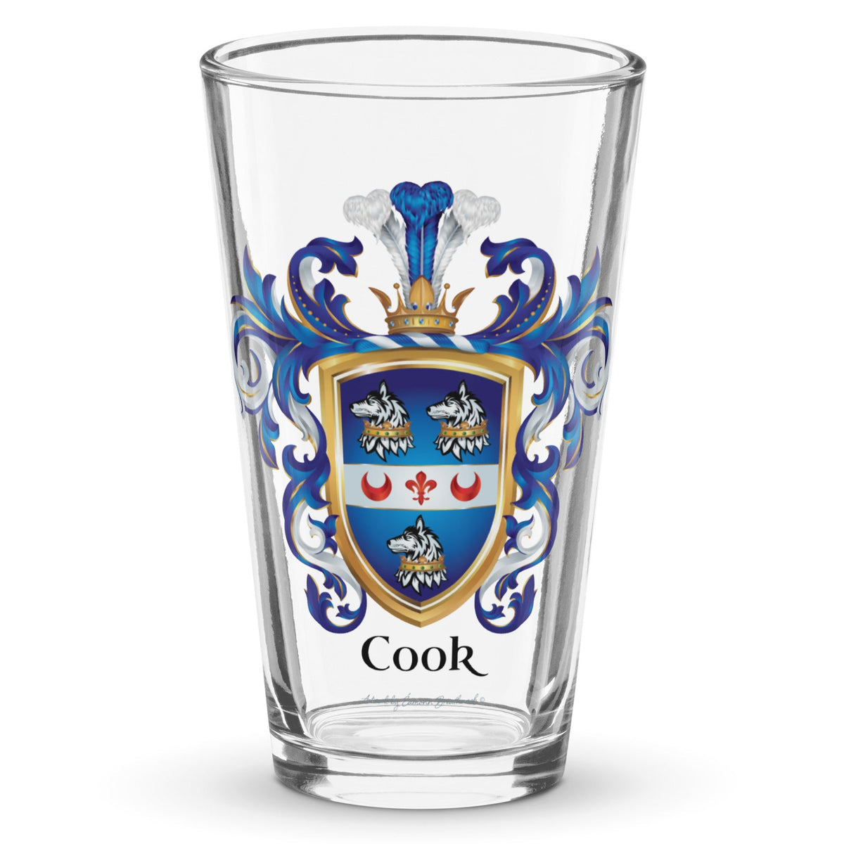 A clear classic pint beer glass on a white background, printed with the Cook Family Crest featuring a blue shield with 3 wolf heads with crowns around their necks and a white band with 2 red crescents and a fleur de lis.