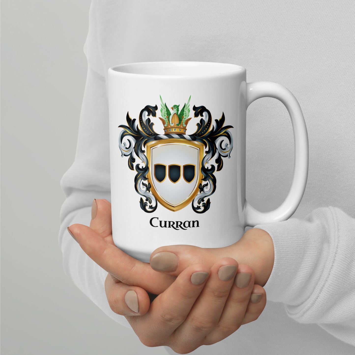A person holding a white ceramic mug with a printed Curran family crest design, shown against a light gray background.