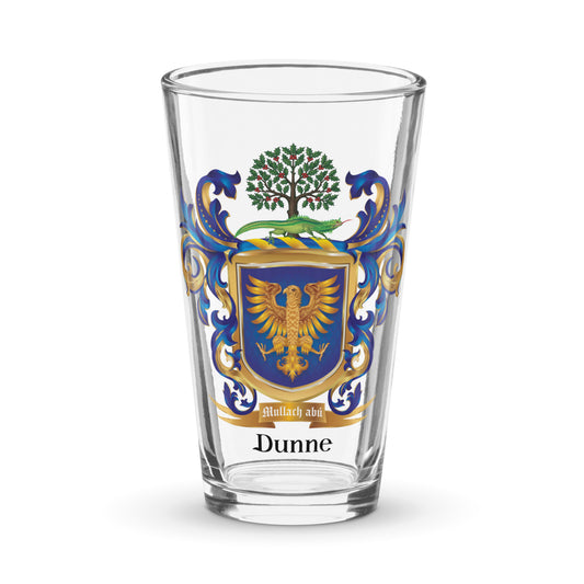 A clear pint glass featuring a printed family crest with a gold eagle, blue and gold shield, green tree, and blue scrollwork, with the name 'Dunne' printed below in black.