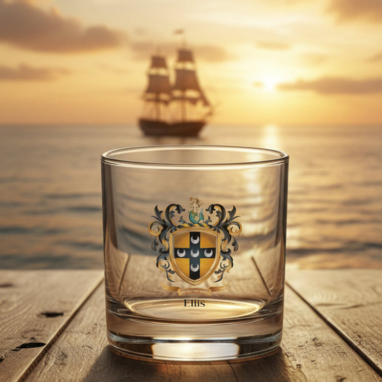 A clear glass rocks tumbler with a printed family crest and the name 'Ellis' below it, shown on a wooden table top with a view of a sailing ship in the background.