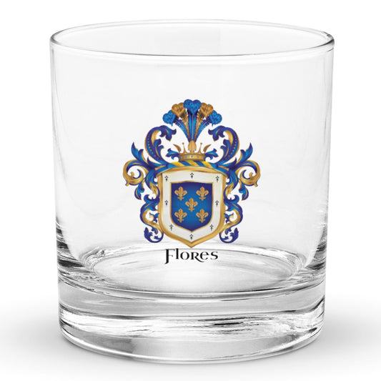 A classic rocks glass on a white background with the Flores Family Crest printed on it. The coat of arms has a blue shield, 5 gold fleur-de-lis, blue and gold mantling, and the name 'Flores' in black heraldic text.