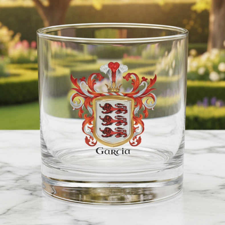 Clear rocks glass with a Garcia family crest and 'Garcia' text in black on a marble table top with a garden in the backgroun