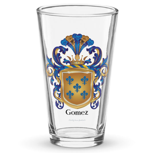 A clear classic pint beer glass on a white background, printed with the Gomez Family Crest featuring featuring 5 blue fleur de lis on a gold shield
