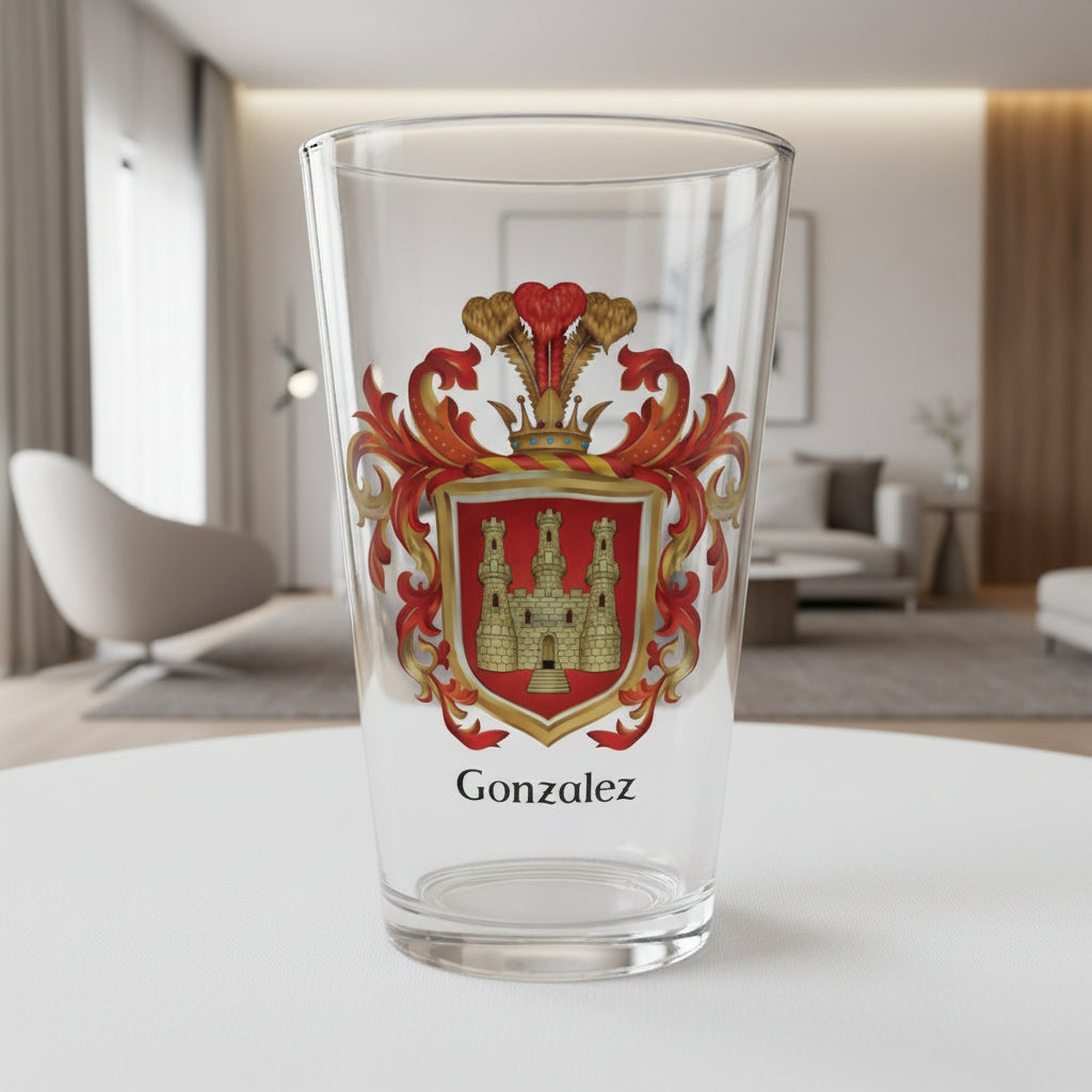 A clear pint glass on a table top with the Gonzalez Family Crest on the front of the glass, featuring a golden castle with 3 towers on a red shield and 'Gonzalez' text in black beneath the coat of arms