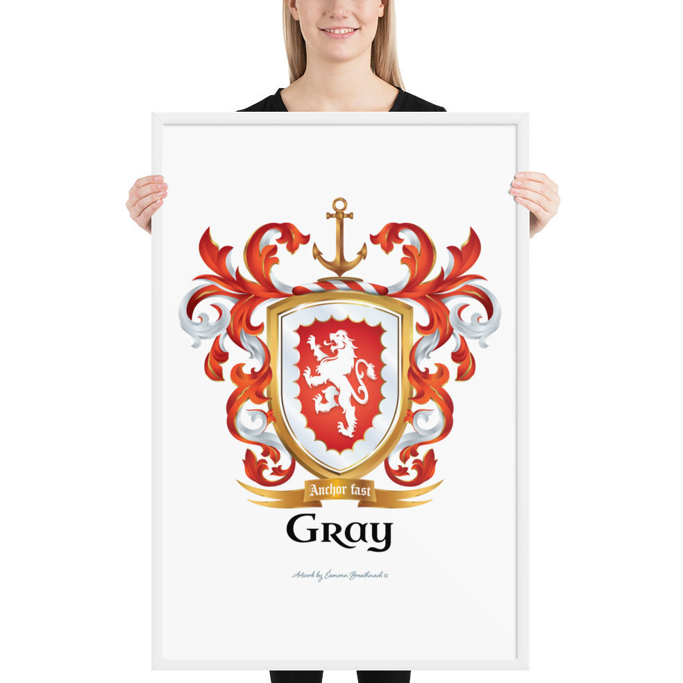 A woman standing in a white background, holding a white framed print of the Gray Family Crest featuring a red shield and white lion and a gold anchor on the crest.