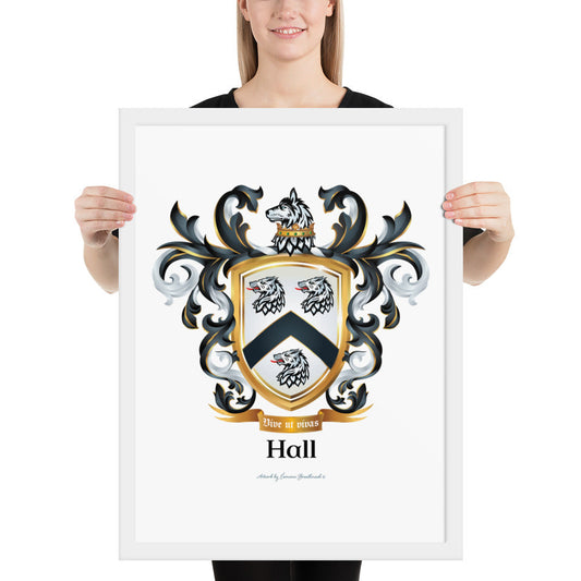 A woman standing in a white background, holding a white framed print of the Hall Family Crest. The crest features a white shield with a black chevron between three wolf heads (two above, one below), topped by wolf with a gold crown around it's neck and surrounded by detailed black and white mantling. The family name and motto appear beneath the shield.