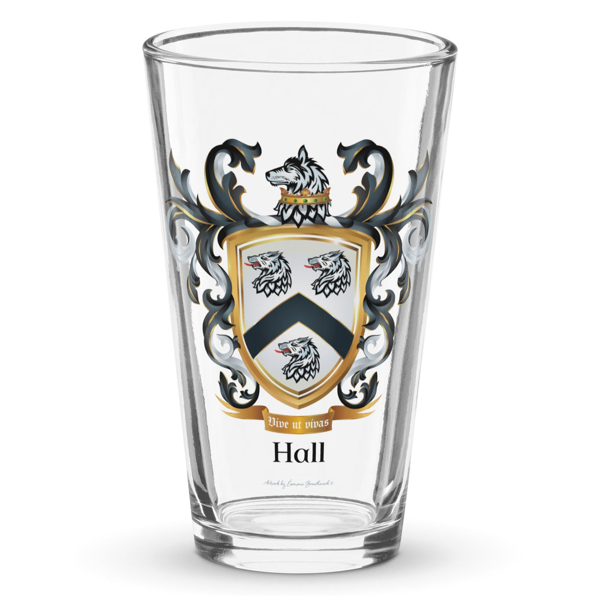 A clear classic pint glass on a white background, printed with the Hall Family Crest. The crest features a white shield with a black chevron between three wolf heads (two above, one below), topped by a gold-crowned wolf with black and white mantling. The family name and motto appear beneath the shield.