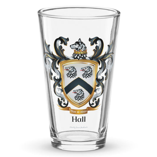 A clear classic pint glass on a white background, printed with the Hall Family Crest. The crest features a white shield with a black chevron between three wolf heads (two above, one below), topped by a gold-crowned wolf with black and white mantling. The family name and motto appear beneath the shield.