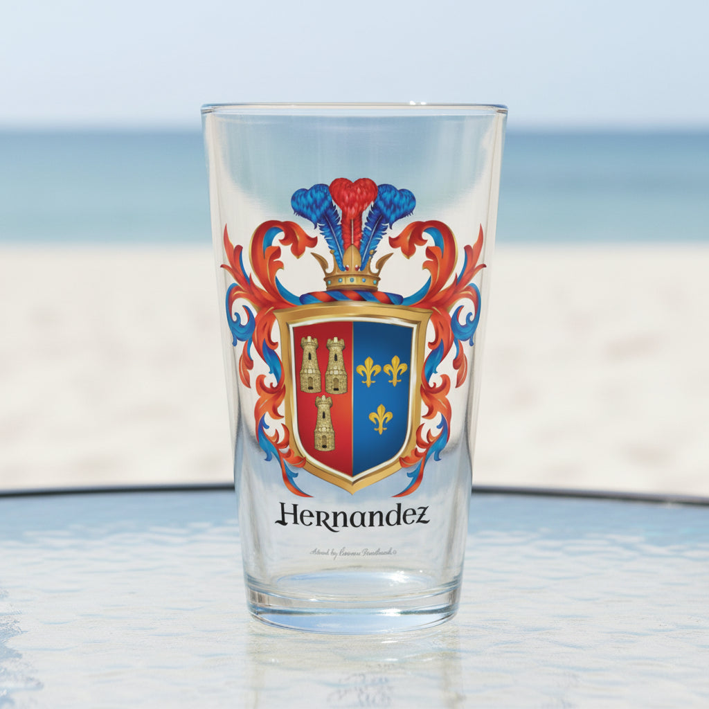 A clear pint beer glass on a white background with the Hernandez coat of arms on the front of the glass featuring a two colour shield, red on left with 3 towers, blue on right  with 3 fleurs-de-lis, and 3 plumes rising from the crown on the crest sitting on top of the shield and the name Hernandez in black slightly stylised typography all surrounded by blue and and red mantling.