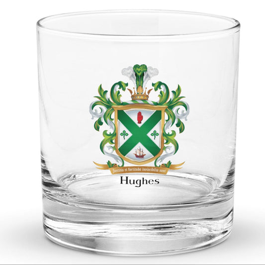 A clear classic heavy base rocks glass on a white background, printed with the Irish Hughes Family Coat of Arms featuring a green and white shield, a gold border, 2 green shamrocks, a s sailing ship, a gold motto scroll reading ‘Justitia et fortitudine invincibilia sunt’, and the name ‘Hughes’ below inheraldic style black text on a white background.