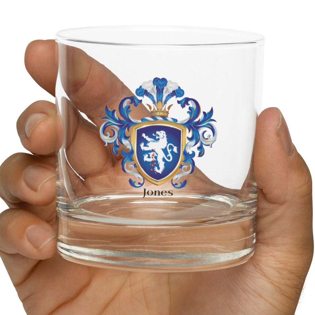 Hand holding a clear Jones Family Crest glass with a coat of arms design on a white background