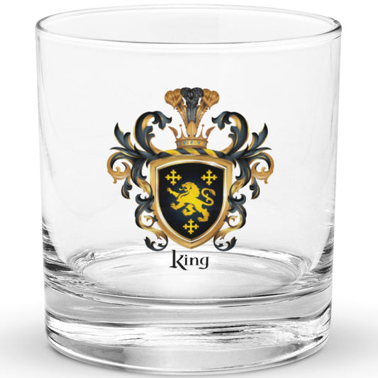 A classic clear rocks glass with a heavy base on a white background and the glass has a King Family Crest printed on it featuring 3 GOLD CROSSES AND A GOLD LION ON A BLACK SHIELD.