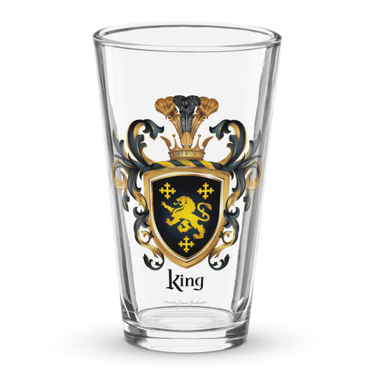 A classic clear pint beer glass on a white background and the glass has a King Family Crest printed on it featuring 3 GOLD CROSSES AND A GOLD LION ON A BLACK SHIELD.