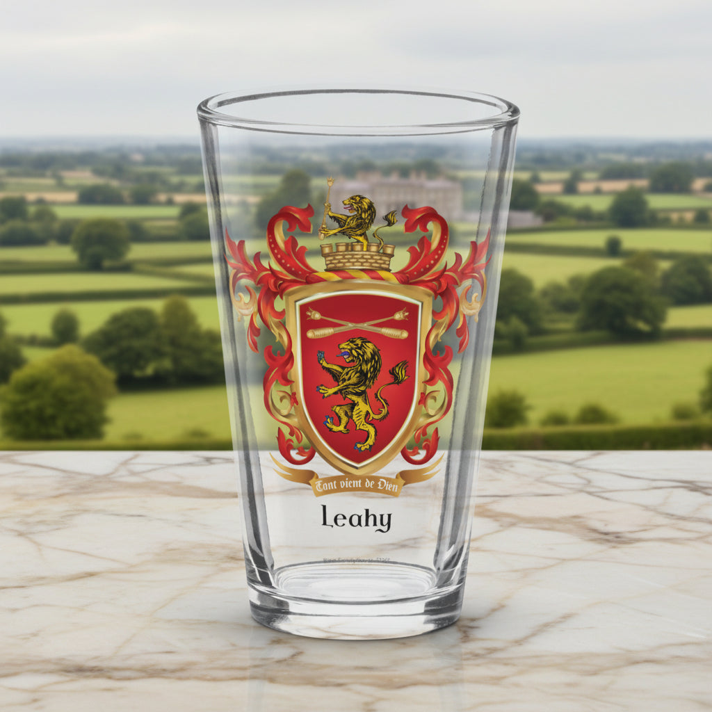A clear pint glass featuring a printed heraldic crest with a red shield, gold lion, red lions, and gold scrollwork, with the name 'Leahy' printed below in black. The glass is photographed on a clean white background with a soft shadow.