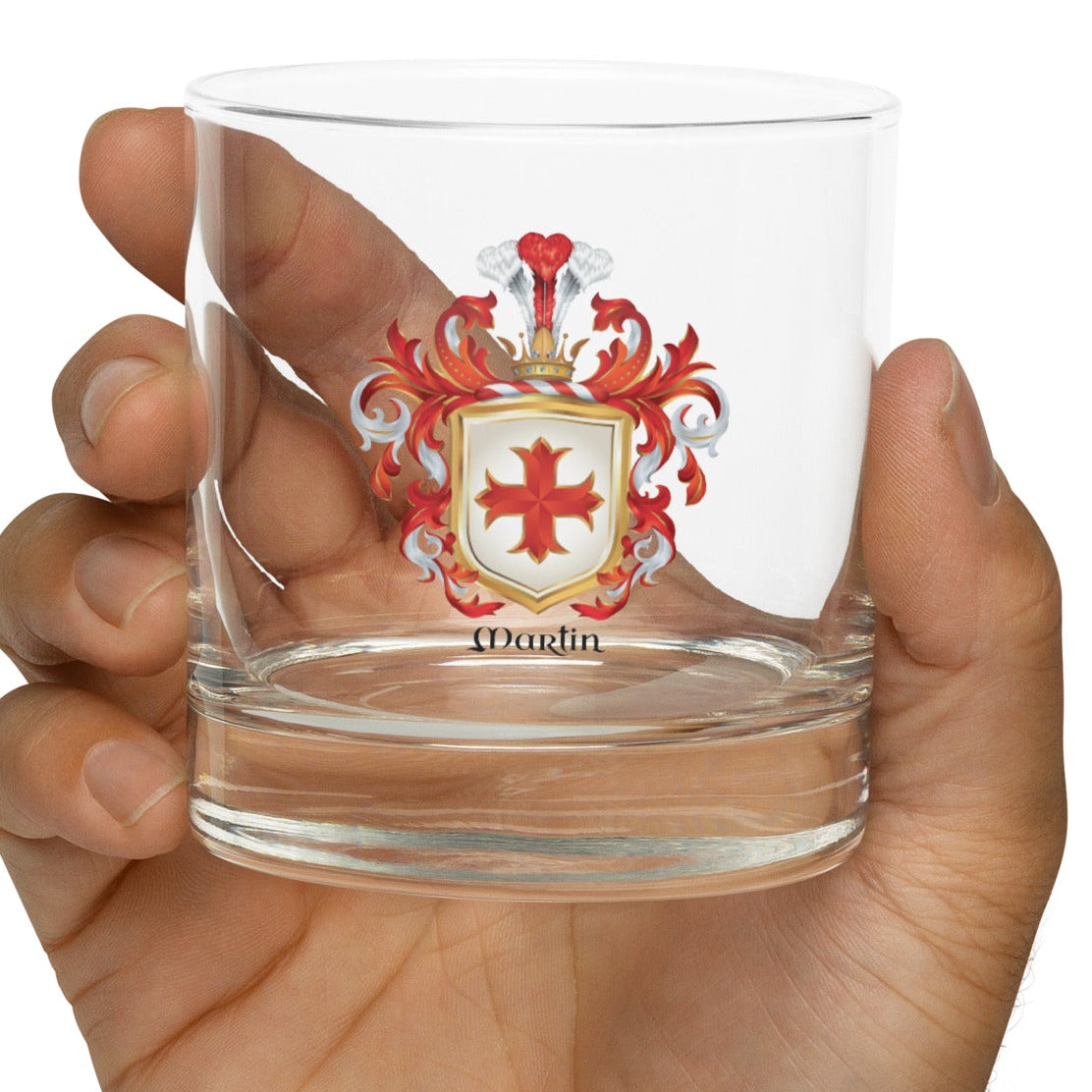 Hand holding a clear glass with a Martin-Family-Crest on a white background