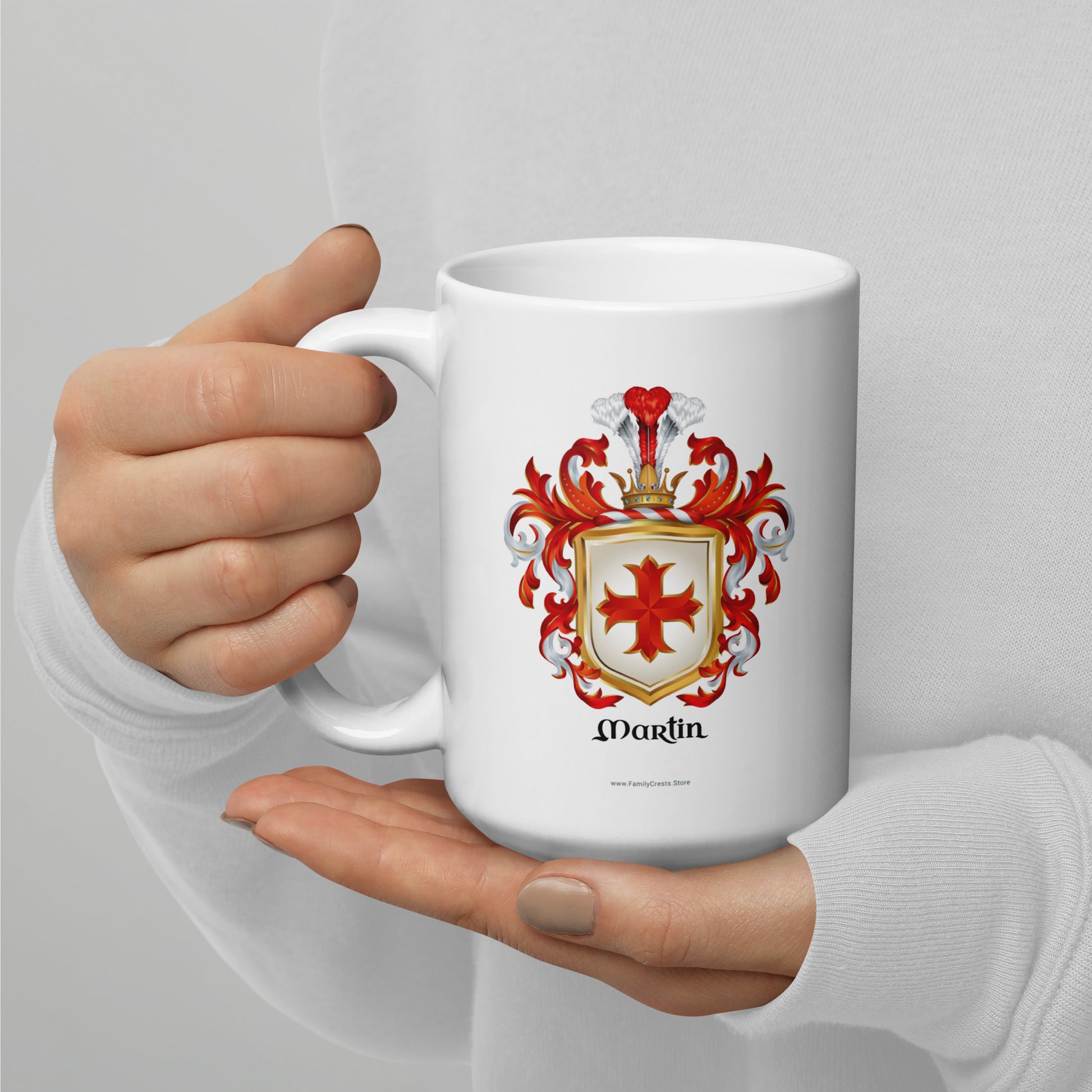 White mug with a Martin Family Crest coat of arms held by a hand on a light gray background