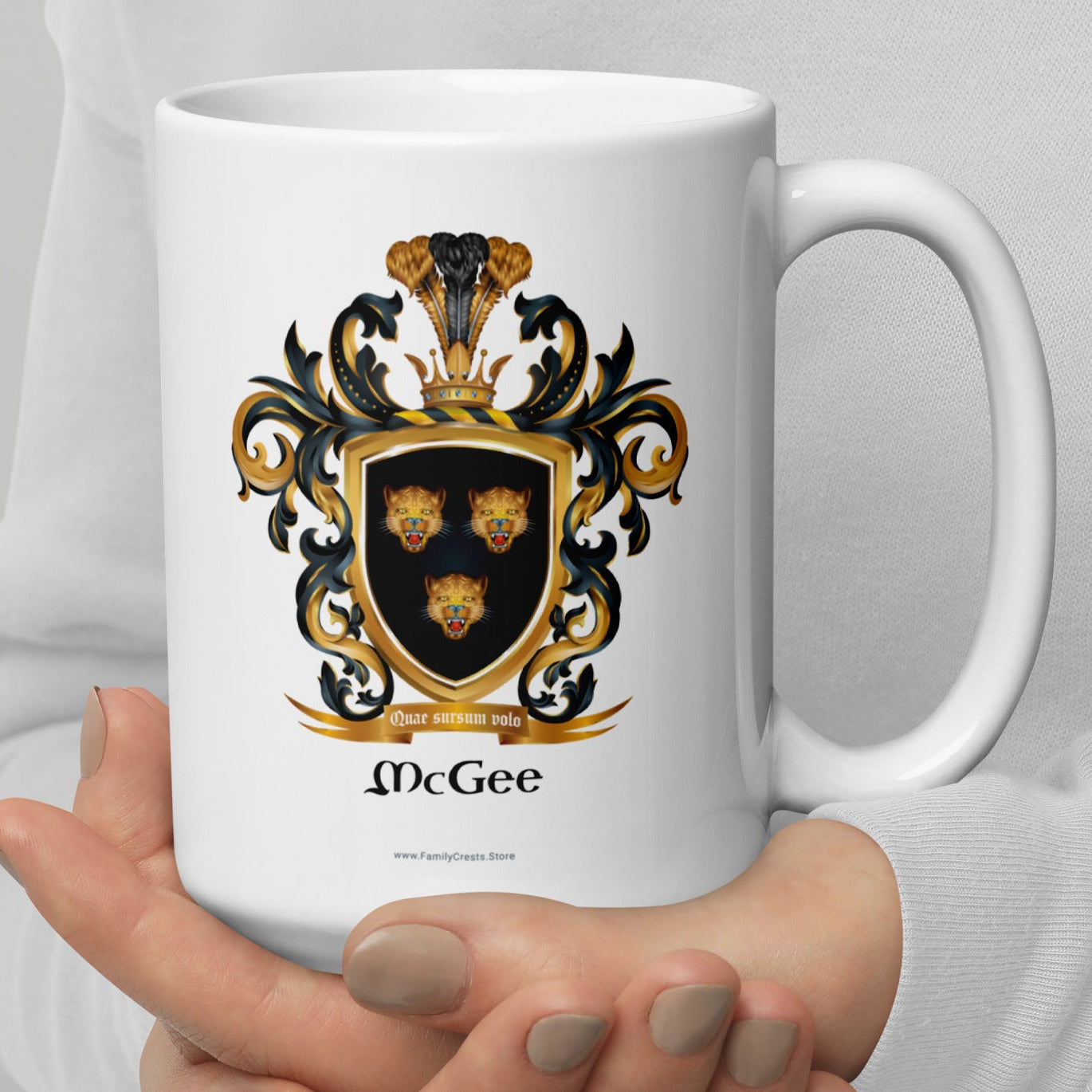 White mug with a McGee family crest design held by a person against a gray background
