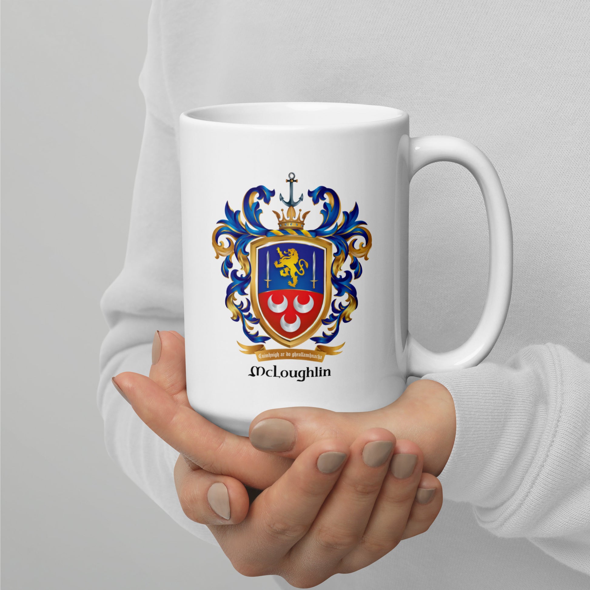 A person in a white sweatshirt holds a white ceramic mug with a colorful McLoughlin family crest printed on the front, set against a plain light gray background.