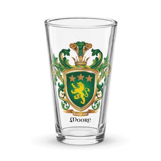 Clear pint beer glass featuring The Moore Family Crest showing a green shield with a gold lion and three gold stars above the lion with the motto and Moore name beloe the shield and a crown above and green and gold mantling all around  on a white background