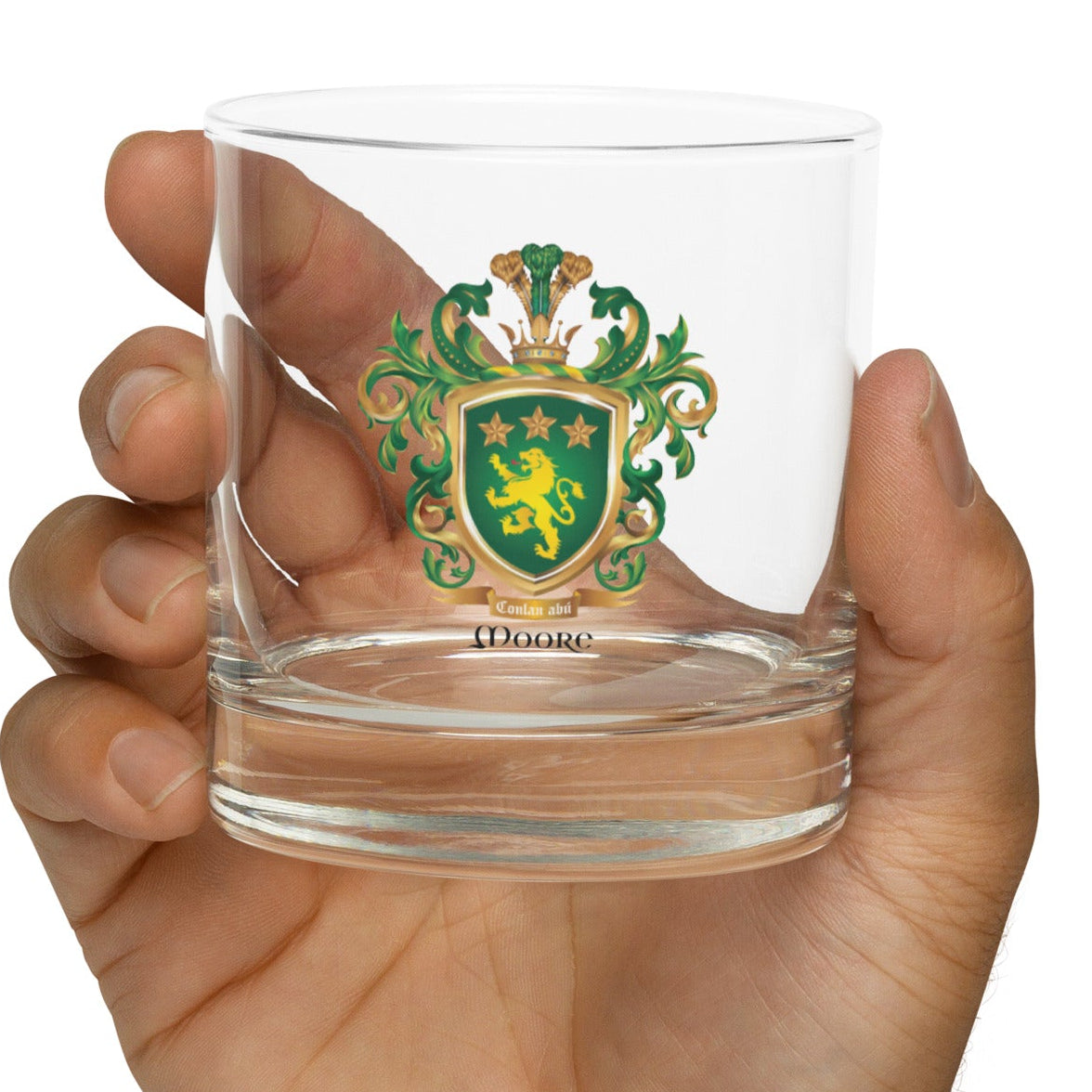 Hand holding aloft a clear rocks glass with the Moore Family Crest displayed on the front