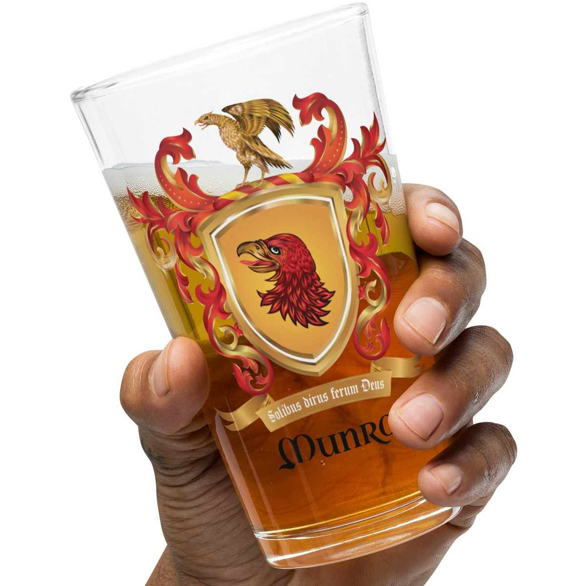 A hand holding a clear pint glass featuring a Gryffindor crest with a red eagle, gold shield, and red flames, partially filled with amber beer, on a white background.
