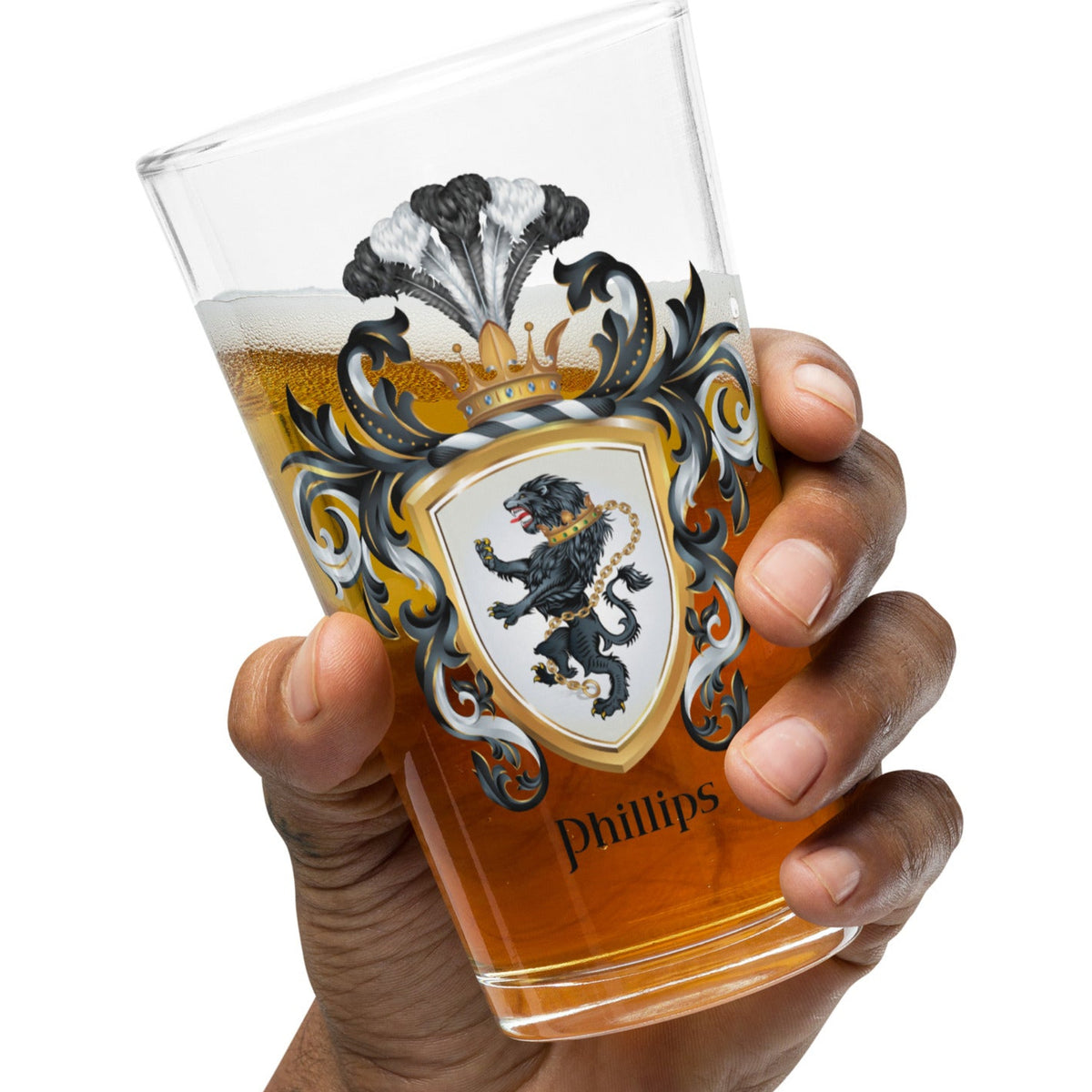 A hand holding a clear pint glass with a printed crest design and the name Phillips, filled with amber beer, against a plain white background.