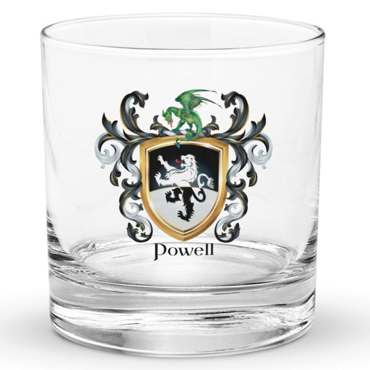 A clear classic heavy base rocks glass on a white background, printed with the Powell Family Coat featuring a black and white shield split with black in the top half, white in the bottom, with a standing lion that also has a white-black color split, and above the lion is a dragon sitting on the crest, and the shield is surrounded with black and white mantling, with the name Powell beneath it in elegant heraldic lettering.