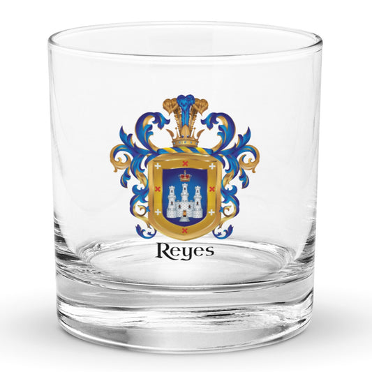 A clear classic heavy base rocks glass on a white background, printed with the Reyes Family Crest which features a blue shield with a white castle and crown.