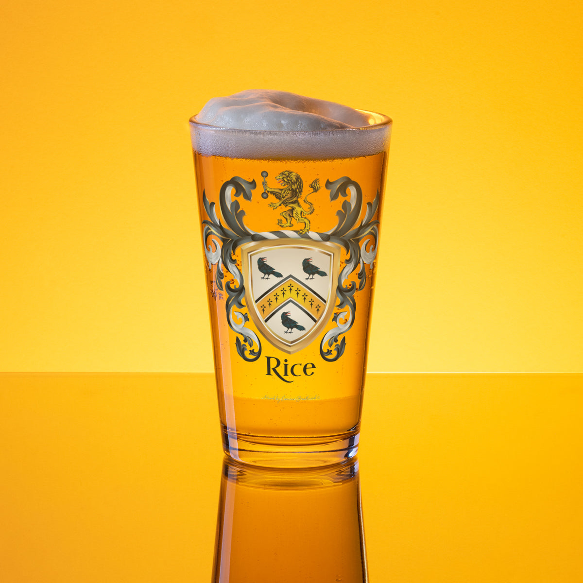 A clear pint glass filled with golden beer and topped with white foam, featuring a Rice Family Crest with birds and the word 'Rice' on the front, set against a bright yellow gradient background with a reflection below.
