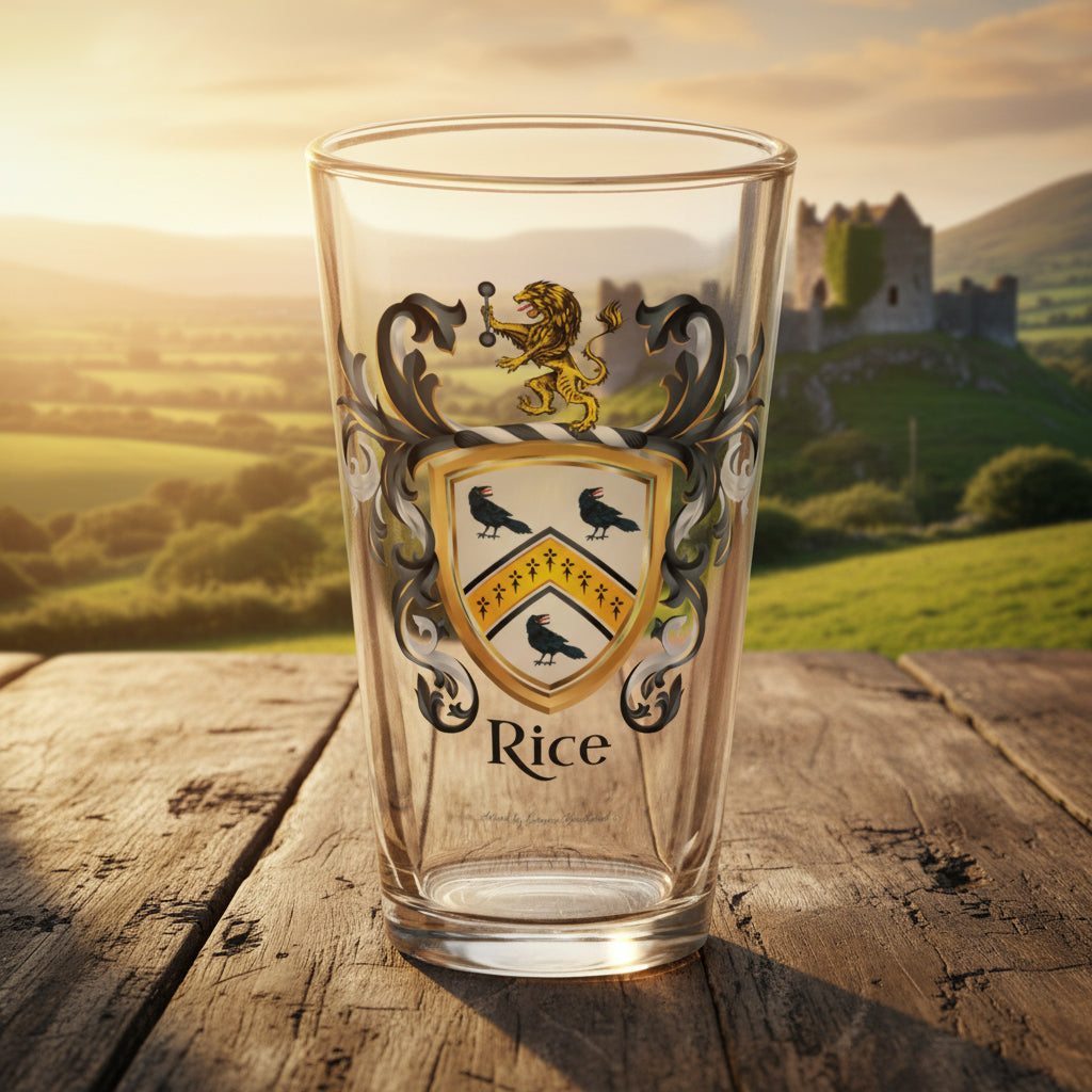 A clear pint glass featuring a custom family crest design with a gold lion, black crows, and the name 'Rice' printed below, shown on a wooden table top with a castle in the distant background.