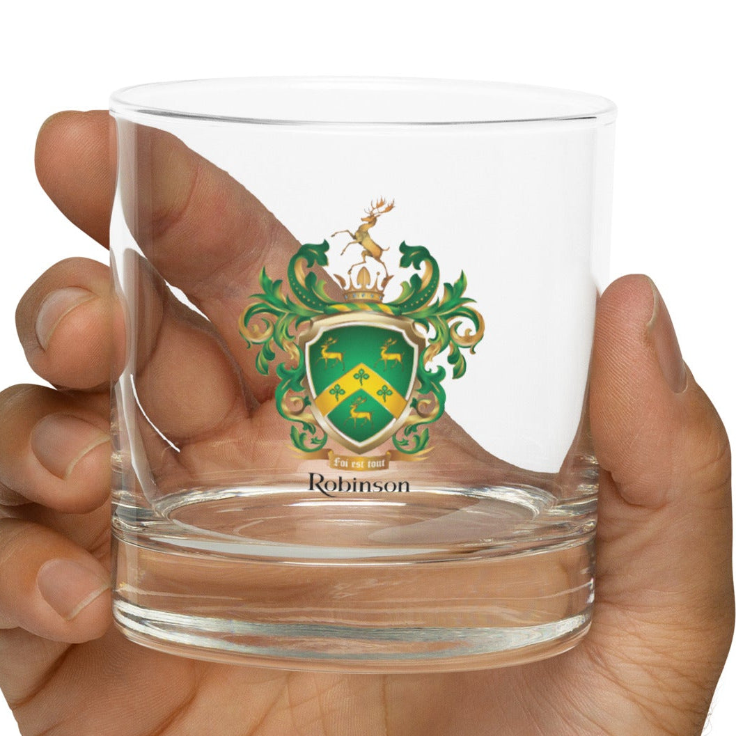 Hand holding a clear Robinson Family Crest glass with a coat of arms design on a white background