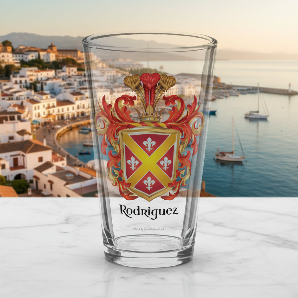 A clear pint glass featuring a printed Rodriguez family crest with the name 'Rodriguez' below it, set against a  background showing a harbour