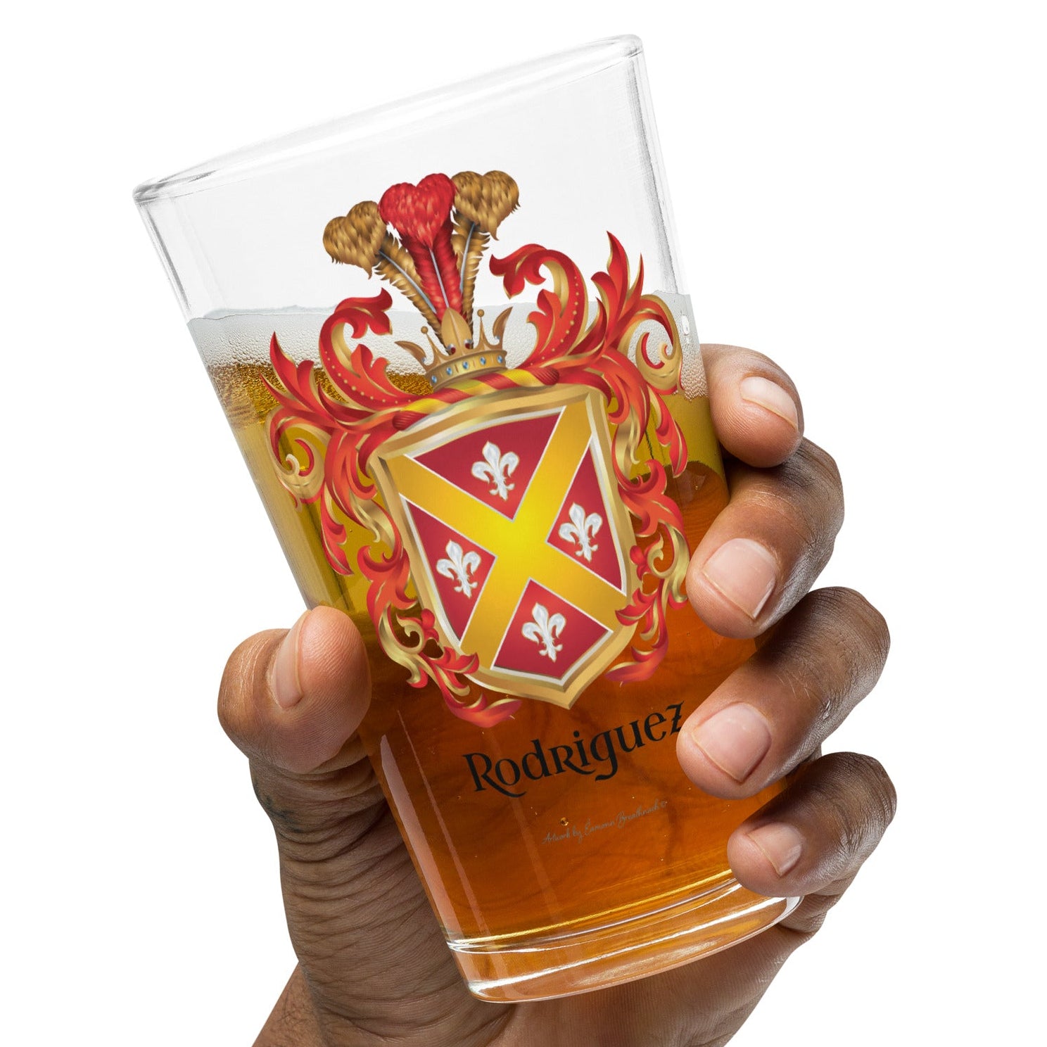 A hand holding a clear pint glass filled with amber beer, featuring a red and gold coat of arms design with the name 'Rodriguez' printed near the bottom, against a plain white background.