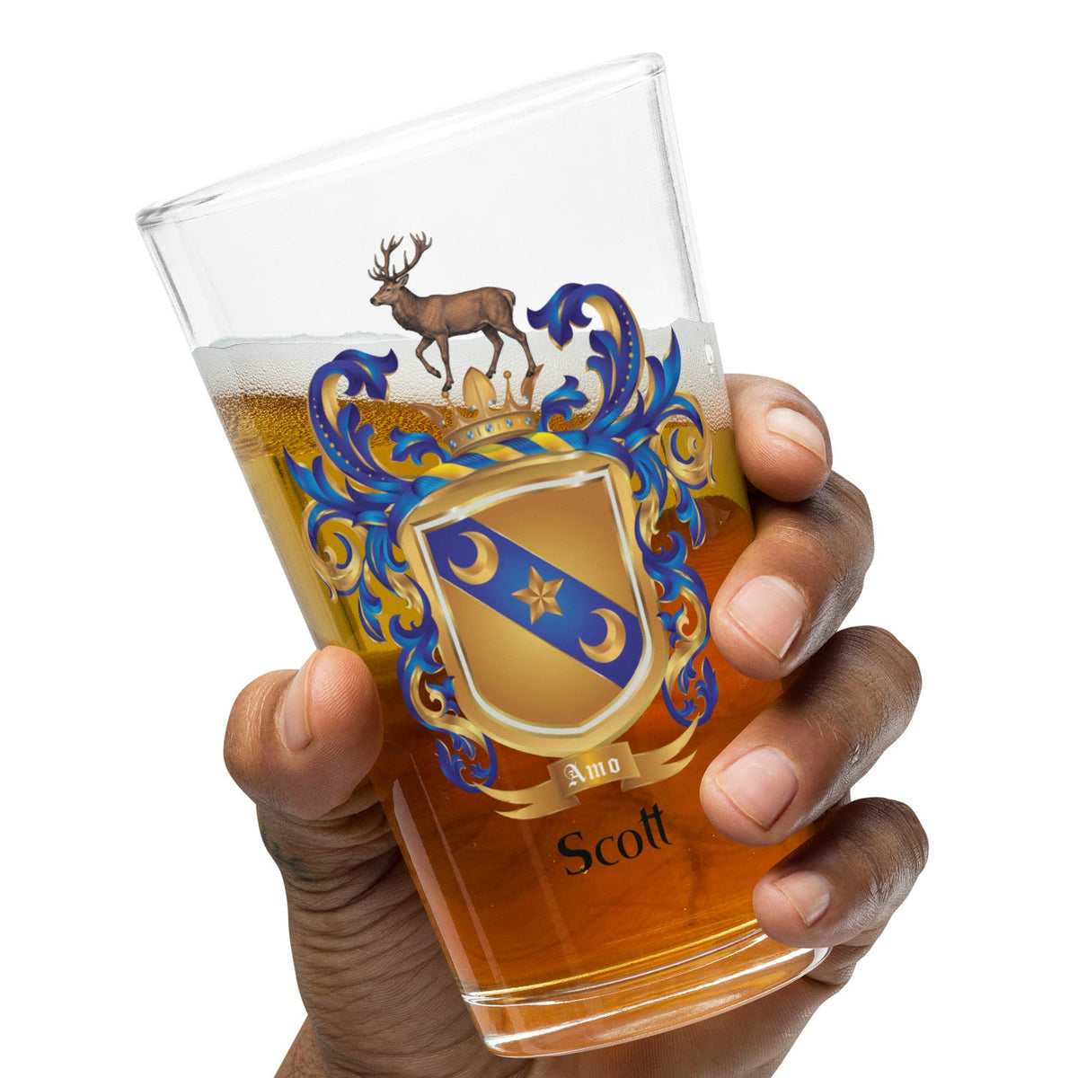 A hand holding a clear Scott Family Crest pint glass filled with amber beer, featuring a personalized Scottish coat of arms crest with a stag and the name 'Scott'.