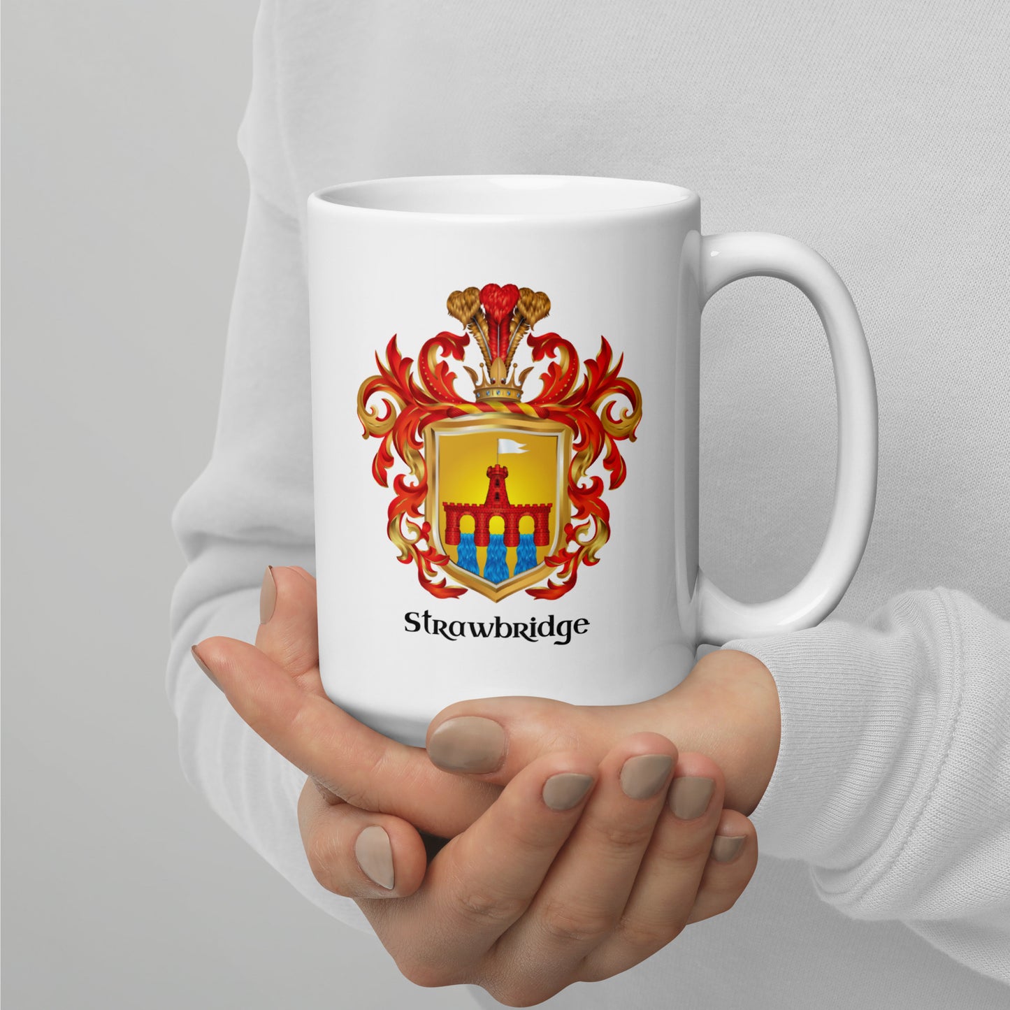 A person in a white long-sleeve top holds a white ceramic mug with a printed Strawbridge coat of arms crest and the word 'Strawbridge' below it.