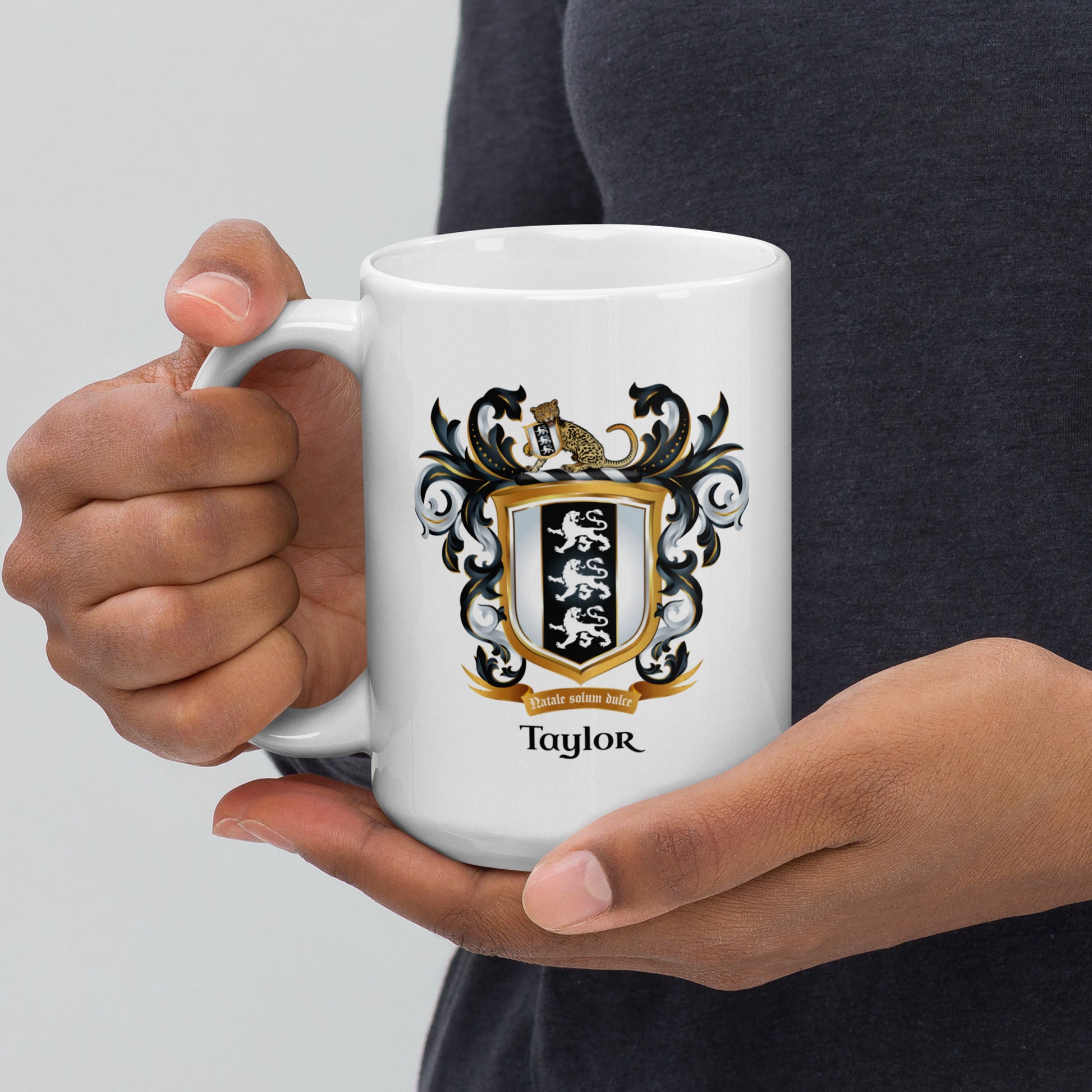 Person holding a white mug with a family crest design and the name 'Taylor' on a plain background